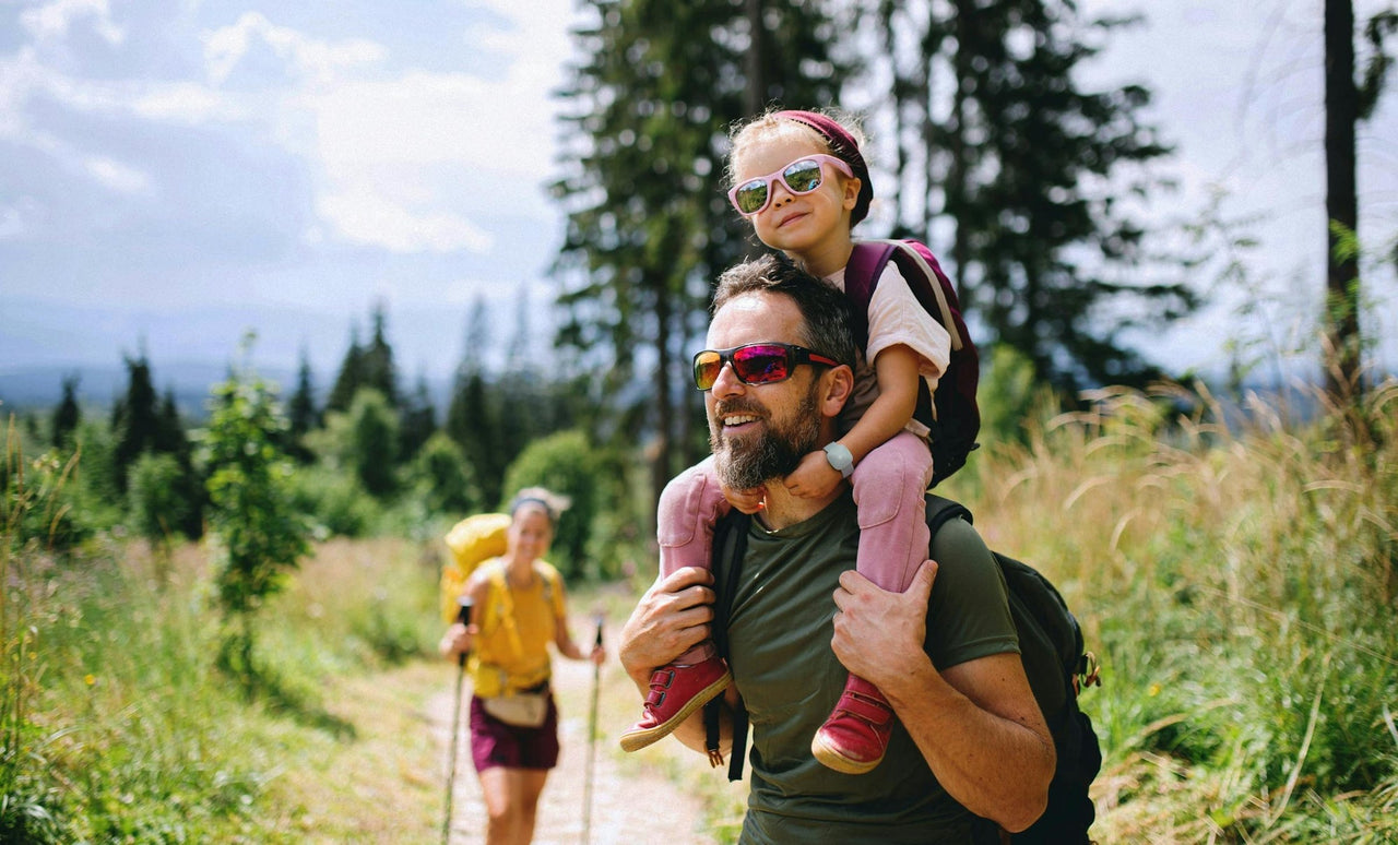 A family enjoying a walk outdoors, with a child riding on a parent’s shoulders.
